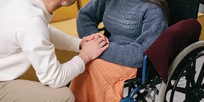 A carer kneeling beside a client seated in a wheelchair